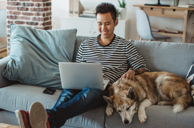 A man his dog on a couch, using his laptop