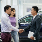 Couple with man shaking hands with a car dealer in front of a vehicle