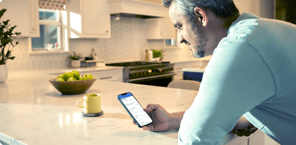 A man leaning on kitchen counter uses smartphone to compare payments and rates