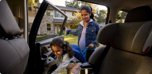 A woman holds the door as her daughter climbs into a car seat