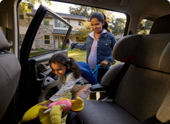 A woman holds the door as her daughter climbs into a car seat