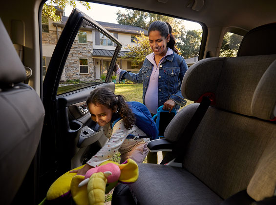 A woman holds the door as her daughter climbs into a car seat