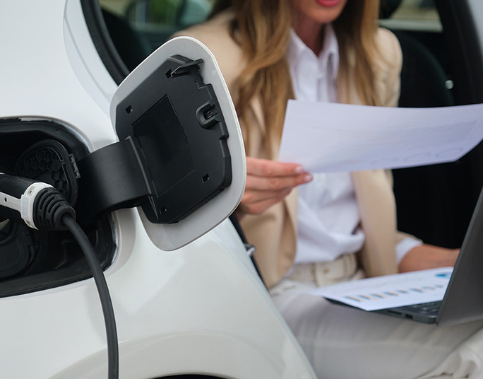 A person holding a paper in front of a charging electric car