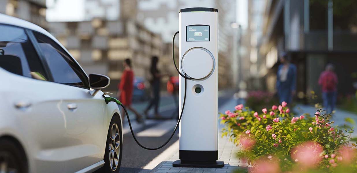 An electric vehicle charging station on a city street with a white car plugged in.