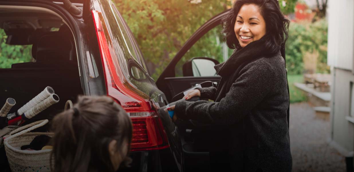 A woman smiling while unloading a black Subaru with an open trunk in an outdoor setting