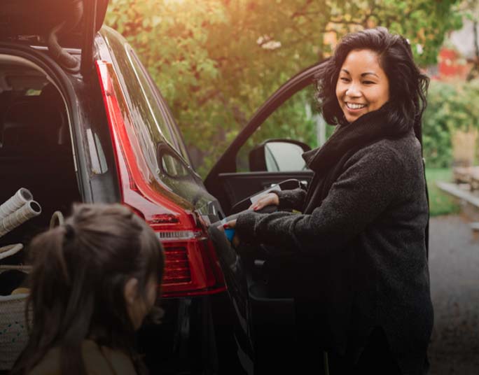 A woman smiling while unloading a black Subaru with an open trunk in an outdoor setting