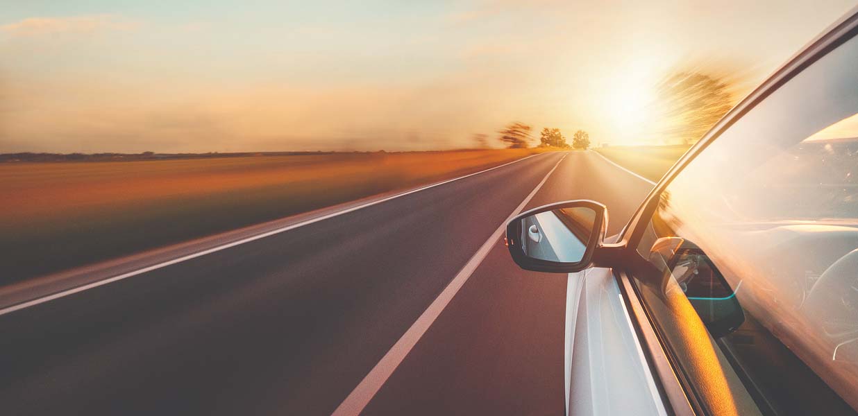 A white car driving on a two-lane road during sunset and surrounding landscape