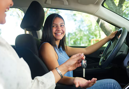 Young woman in driver's seat accepting keys of her first car 