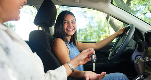 Young woman in driver's seat accepting keys of her first car