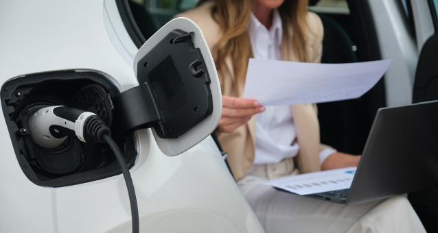 A person holding a paper in front of a charging electric car