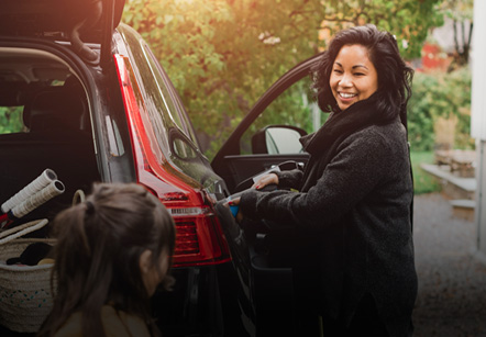 A woman smiling while unloading a black Subaru with an open trunk in an outdoor setting