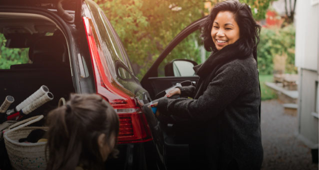 A woman smiling while unloading a black Subaru with an open trunk in an outdoor setting