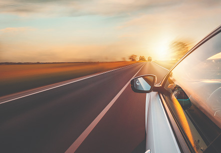 A white car driving on a two-lane road during sunset and surrounding landscape