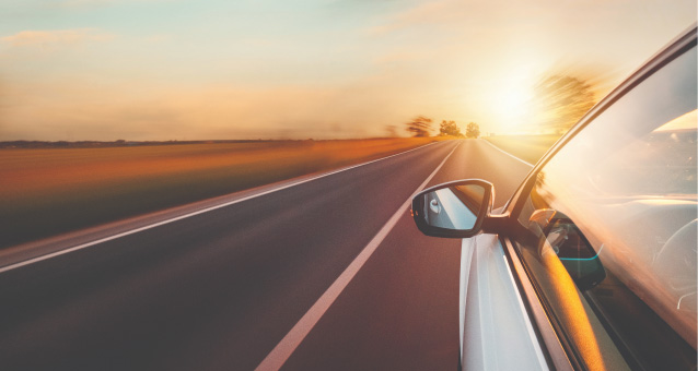 A white car driving on a two-lane road during sunset and surrounding landscape