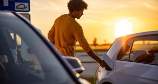 A man attaching the charger from an electric vehicle charging port in front of a sunset