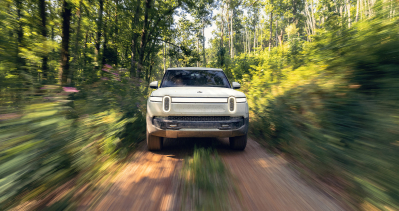 A Rivian electric vehicle speeds through a path in the forest