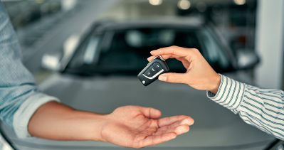 A woman hands a pair of keys to a man in front of a vehicle