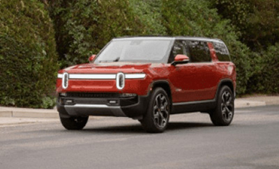 A Rivian R1S driving in front of greenery 