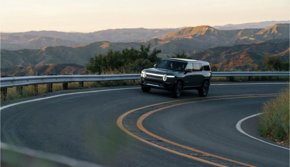 A Rivian R1S driving around a bend on a scenic mountain road