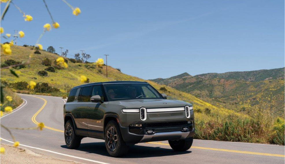 Rivian R2 driving on a scenic mountain road
