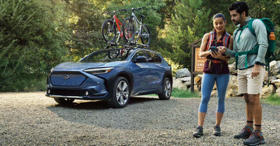 A Subaru electric vehicle drives up a dirt road through a forest