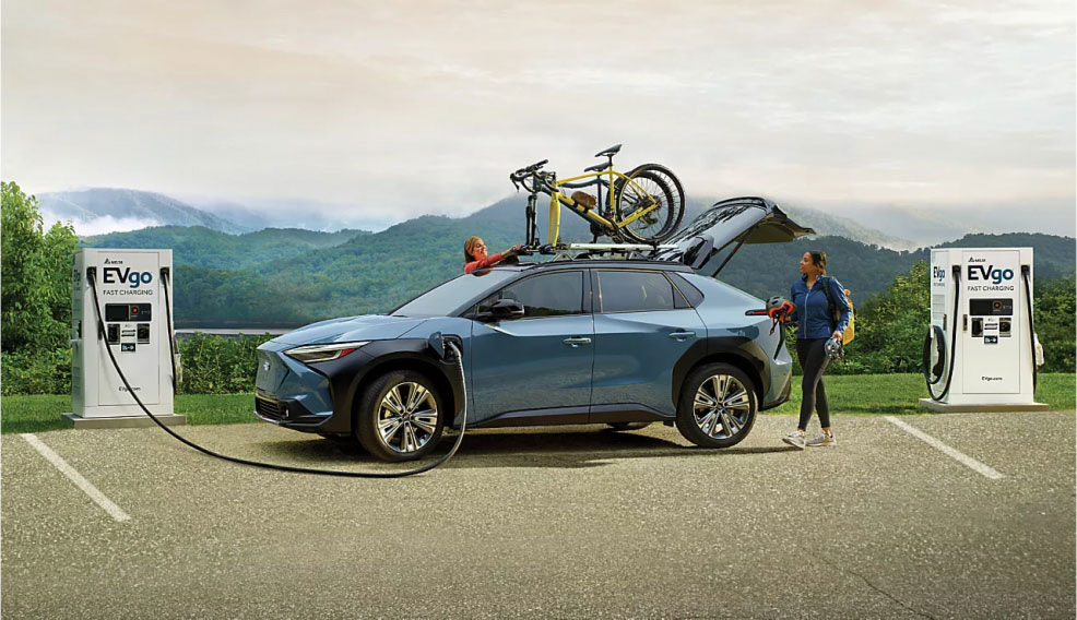 Two people pack up and secure bikes to their vehicle's rooftop as it charges in a mountain range