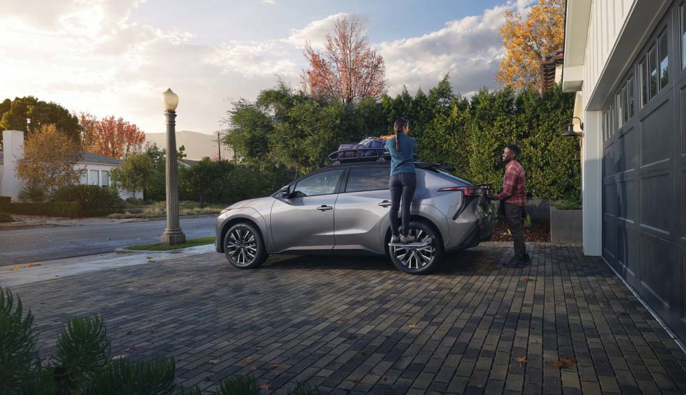 Two people beside a silver Subaru parked in a brick-paved residential driveway