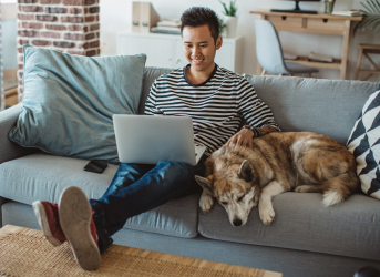 A man his dog on a couch, using his laptop